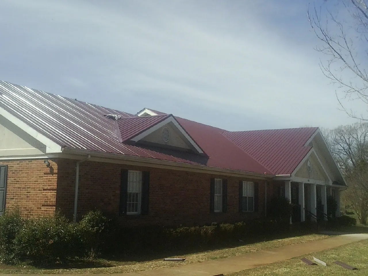 Red metal roof with gabled entries on a long brick building, from a Hail Damage Roof Repair job in Smithville