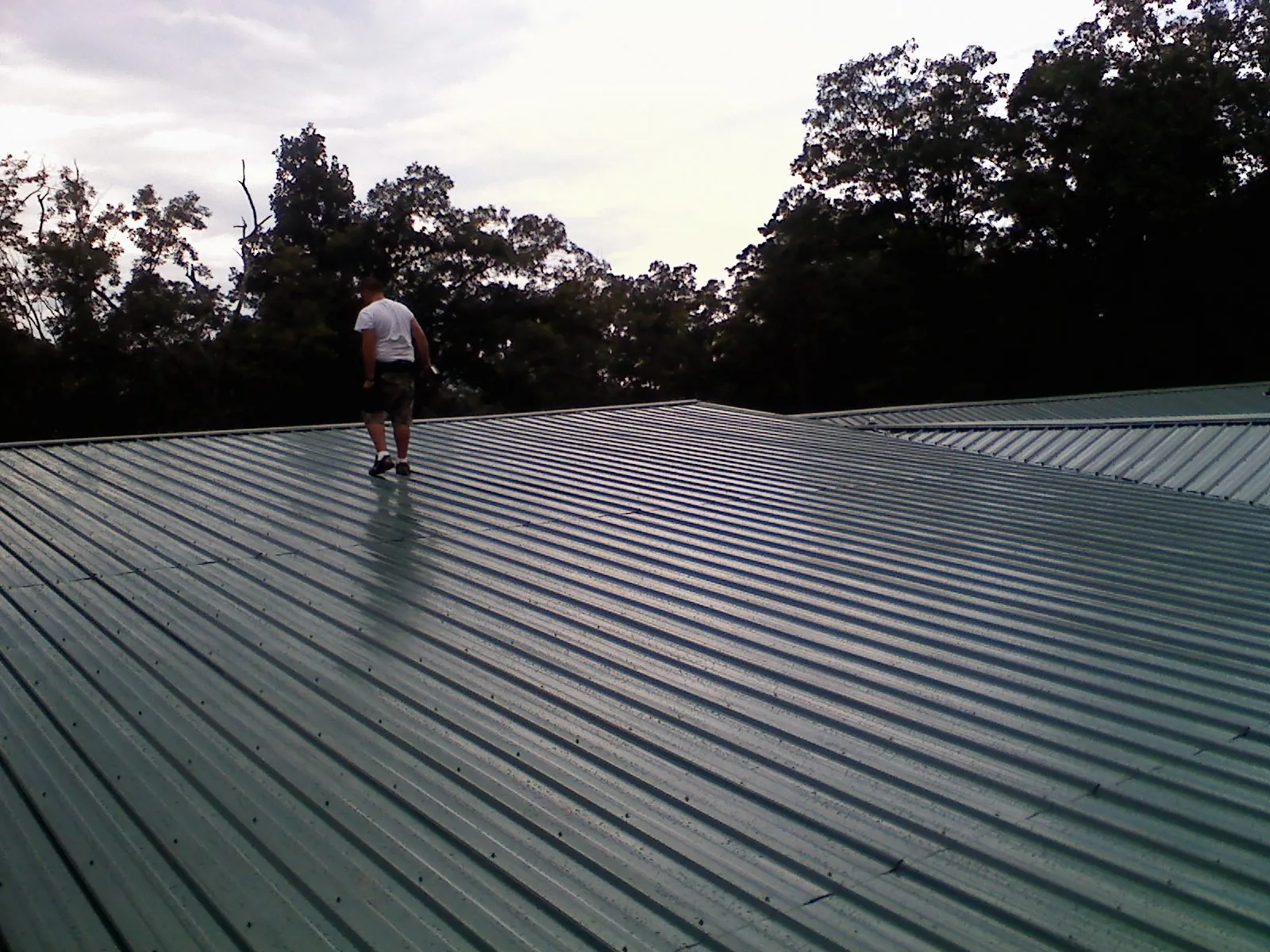 Roofer walking a wide expanse of new green metal roofing in Smithville